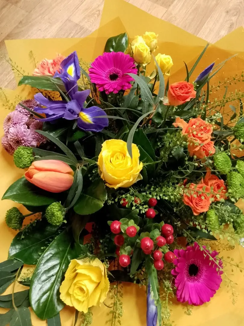 Hand tied bouquet on gold wrapping paper: purple iris, pink and magenta gerbera, yellow roses, orange tulip, green chrysanths and red hypericum berries